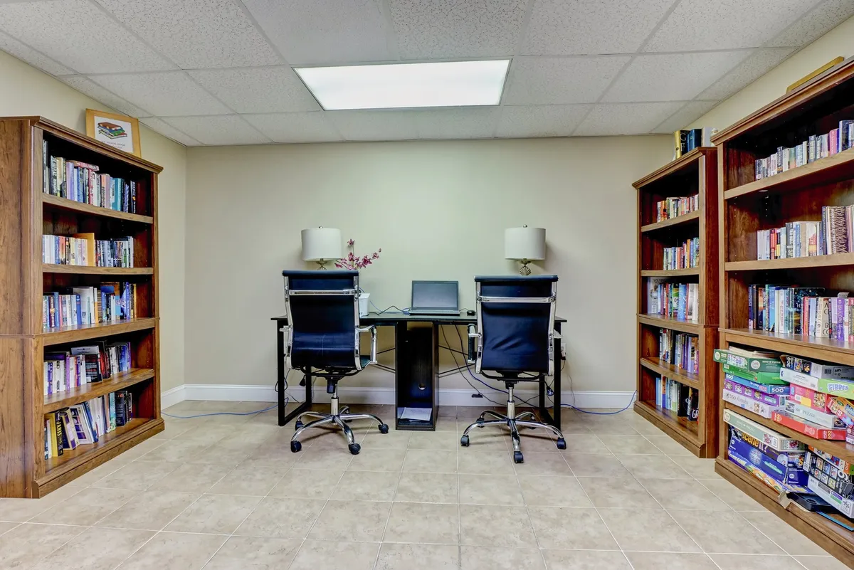 A serene business center interior with bookshelves, desks, chairs, and a computer, providing a quiet, productive space for remote work or study. The atmosphere is calm and conducive to focus, with thoughtful workspace arrangements.