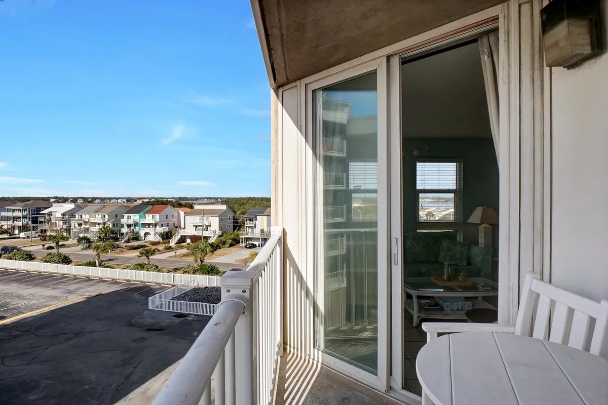The image features a spacious balcony equipped with outdoor furniture, overlooking the ocean and surrounding homes. The scene suggests a relaxed atmosphere, ideal for enjoying coffee, reading a book, or simply soaking in the sunrise over the horizon. The view highlights the balcony's connection to both the sky and sea, reinforcing its role as an extension of indoor living space.