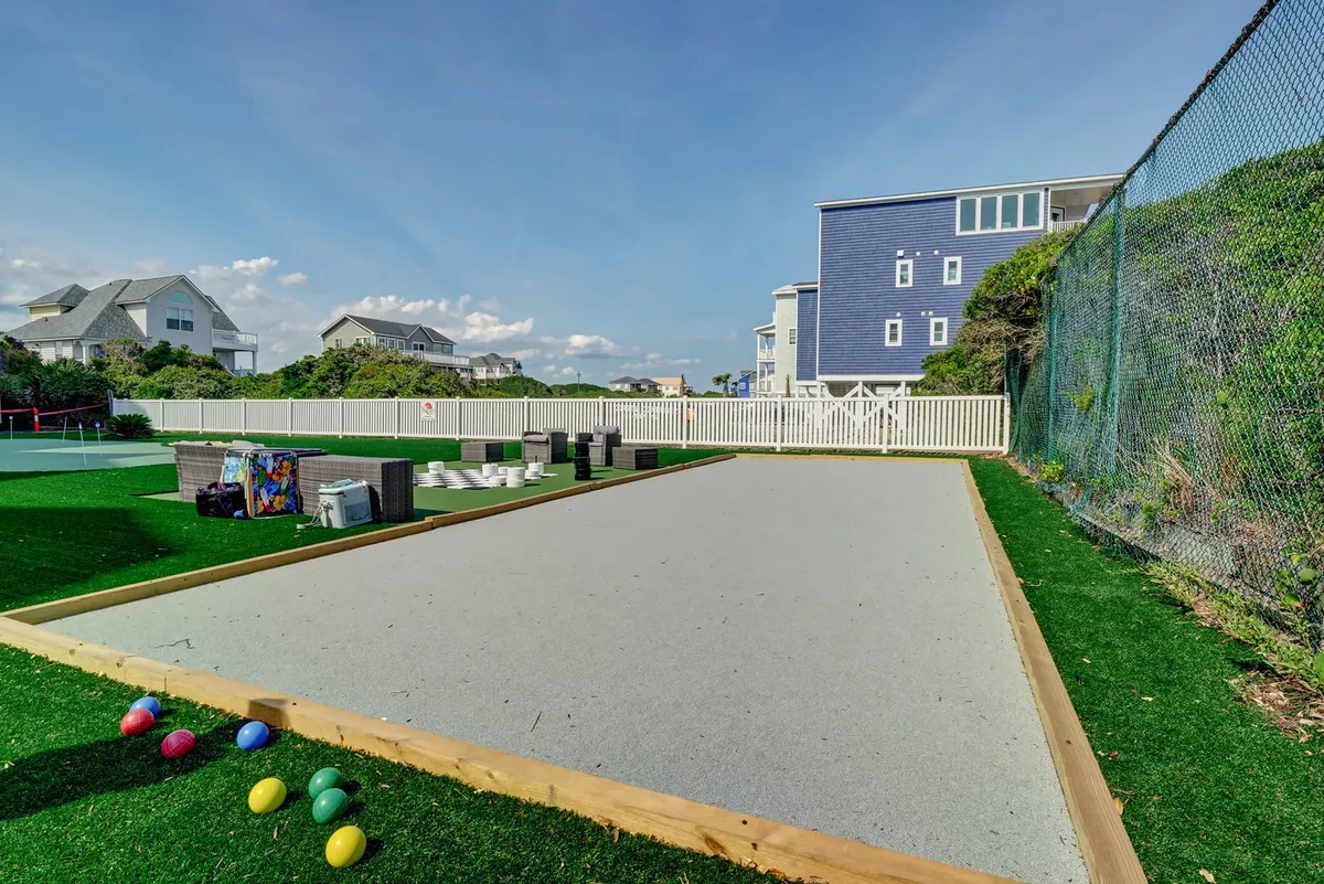 An inviting bocce ball court set on fresh green grass, surrounded by colorful bocce balls, neighborhood houses, and ample seating. The open-air environment is bright and relaxed, promoting outdoor leisure and light social interaction.