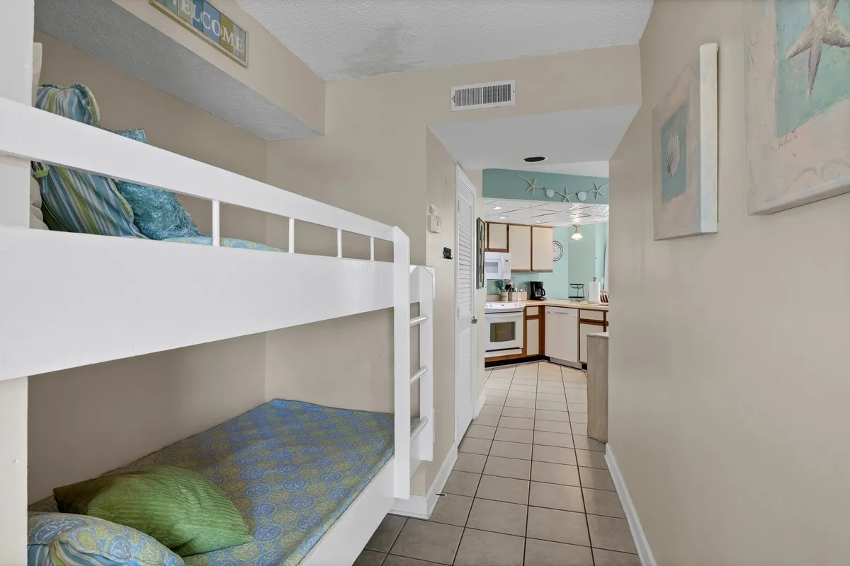 A playful bunk area featuring twin-size bunk beds with cheerful bedding, decorative wall art, and a partial view of the kitchen in the background, highlighting the space's connection to family life and comfort.