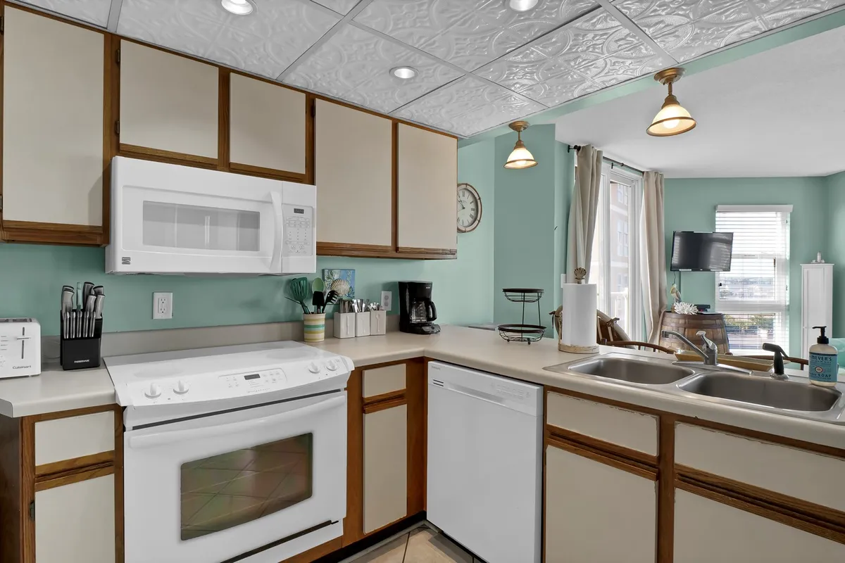 A cozy kitchen with modern appliances, a sink, countertop, and a window that brings in natural light. The layout encourages social cooking and easy interaction with adjacent areas.