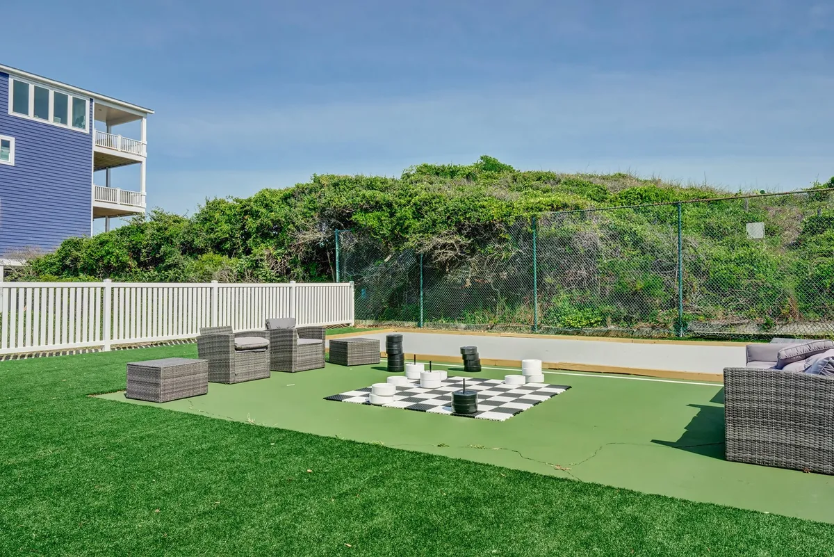 A large outdoor chessboard set on lush green grass with comfortable seating nearby, all under open sky. The playful area invites couples to relax, play games, or engage in lighthearted moments outside together.