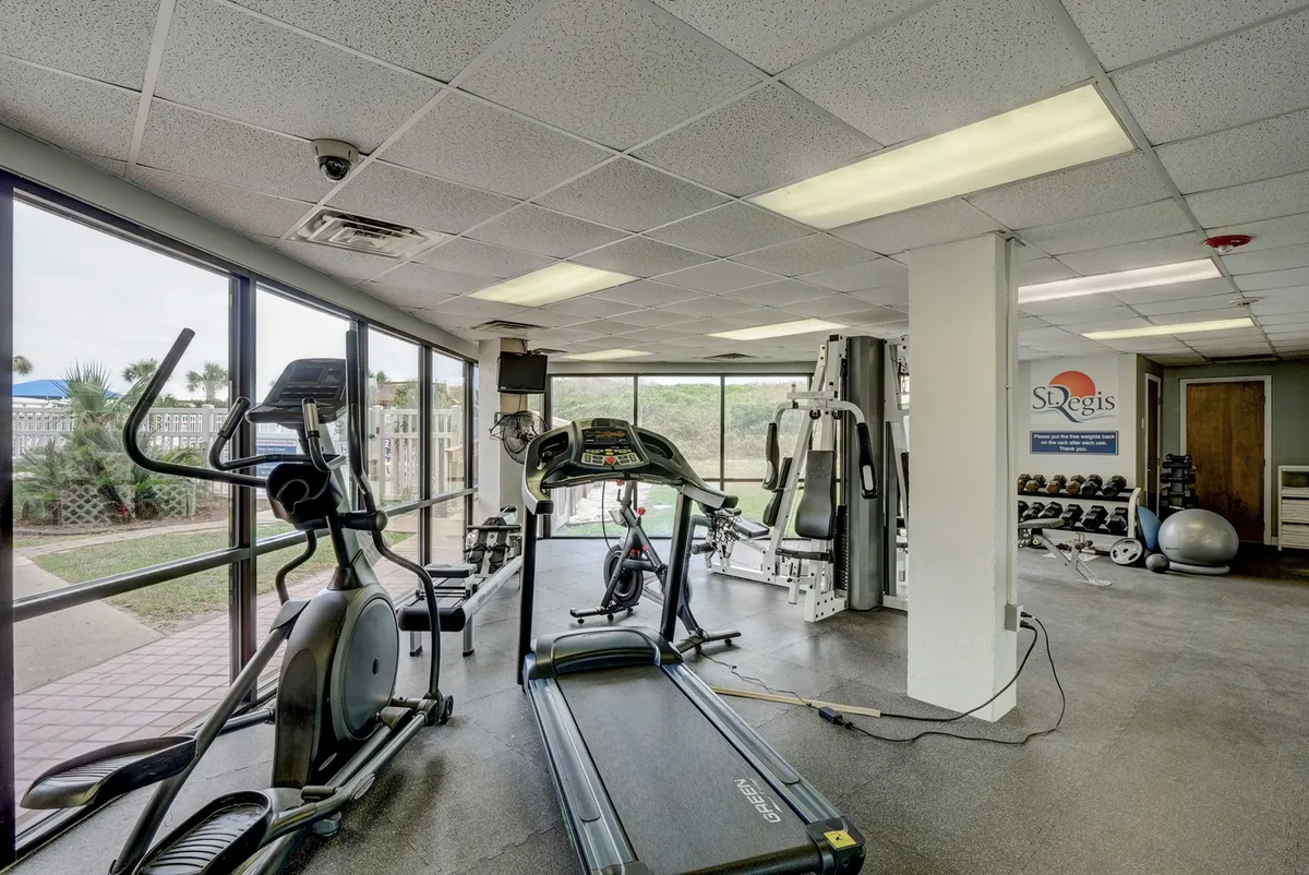 A bright, spacious fitness center featuring treadmills, elliptical machines, weight training equipment, and large windows that flood the space with natural light. The setup suggests opportunities for both solo workouts and group fitness classes.