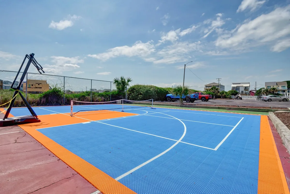 An exterior view of a basketball court complete with a tennis net and lush surrounding greenery. The open layout invites both casual play and organized matches among friends or family.