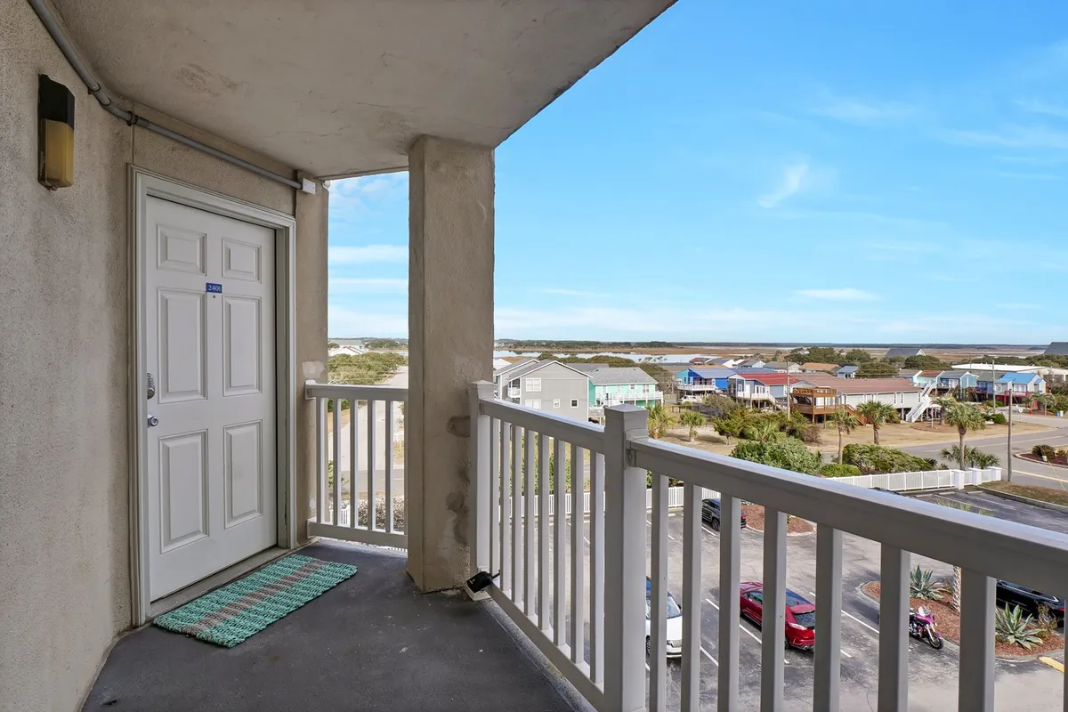 A cozy private balcony with a railing overlooks neighboring houses and a broad sky. The scene suggests peaceful moments of relaxation, with space for seating and plenty of natural light, perfect for enjoying morning coffee or watching sunrises together.