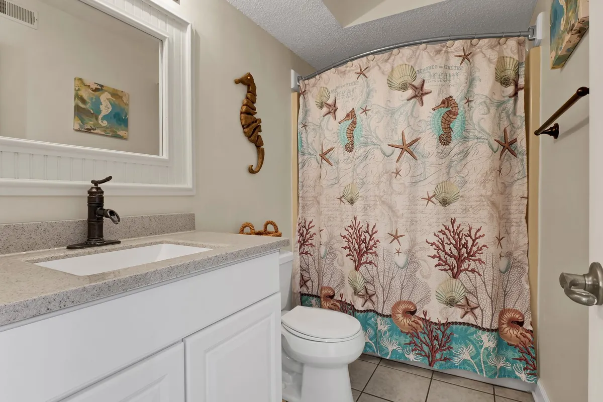 A light-filled bathroom with a modern sink and faucet, a decorative seahorse accent on the wall, and a seashell-patterned shower curtain—offering a fresh, beach-inspired ambiance.
