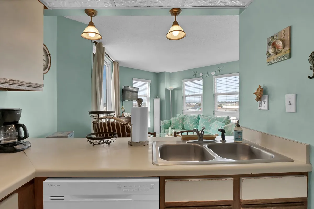 An inviting open-concept space with the kitchen sink in the foreground, a spacious dining area, and a living area with large windows that fill the room with natural light and reveal ocean views.